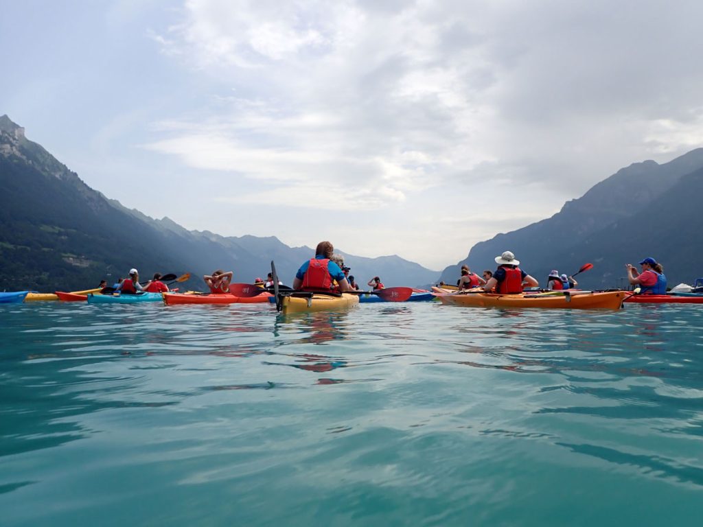 A group kayaks on a lake with mountains in the background