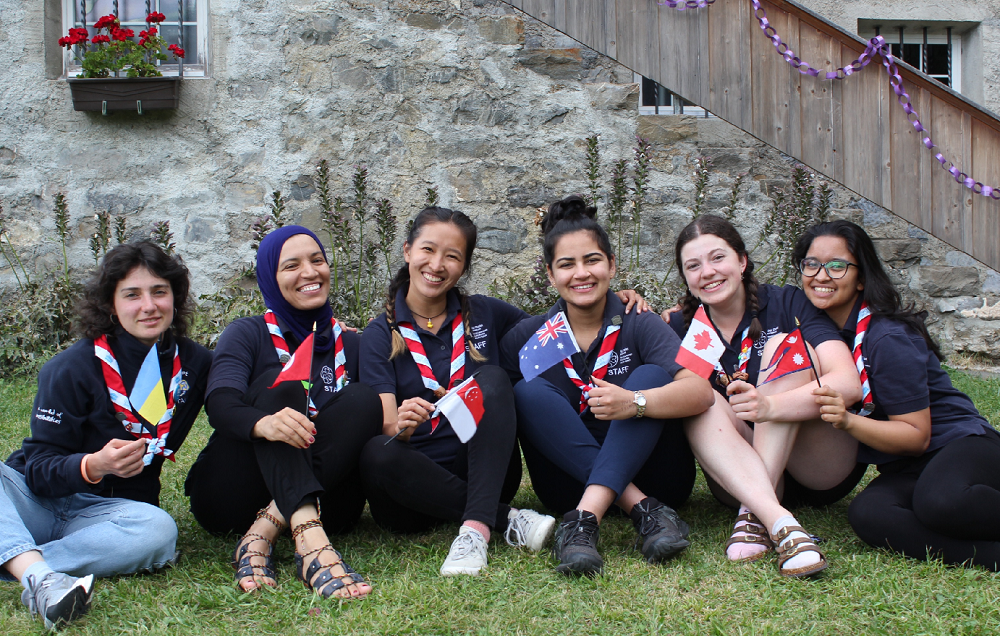 6 staff members sitting on grass holding their homecountry flags