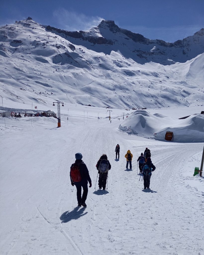A snowy alp with five people walking away from the camera