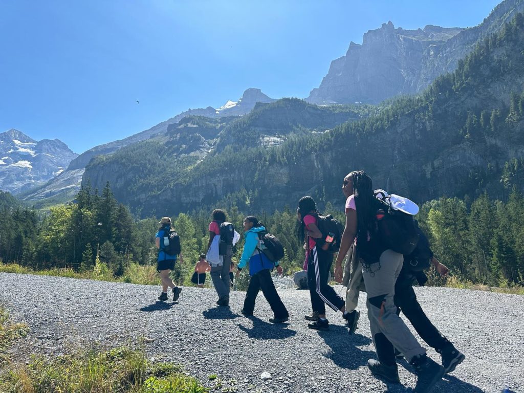 A group of girls and young women hiking in the mountains on a gravel path. Blue sky and sunny weather.