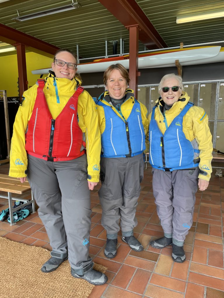 Three women of different ages in bright yellow kayaking dry suits and bouyancy aids.