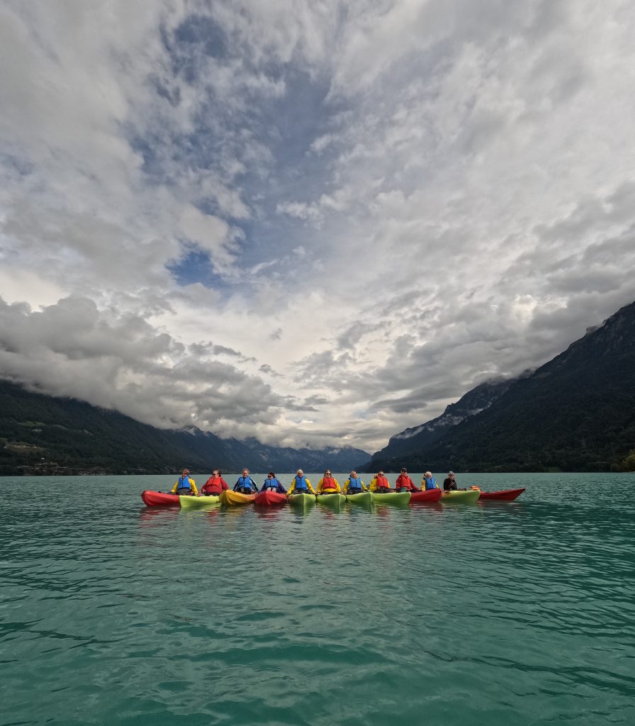 A group of women in colourful kayaks on a blue kale with mountains in the background