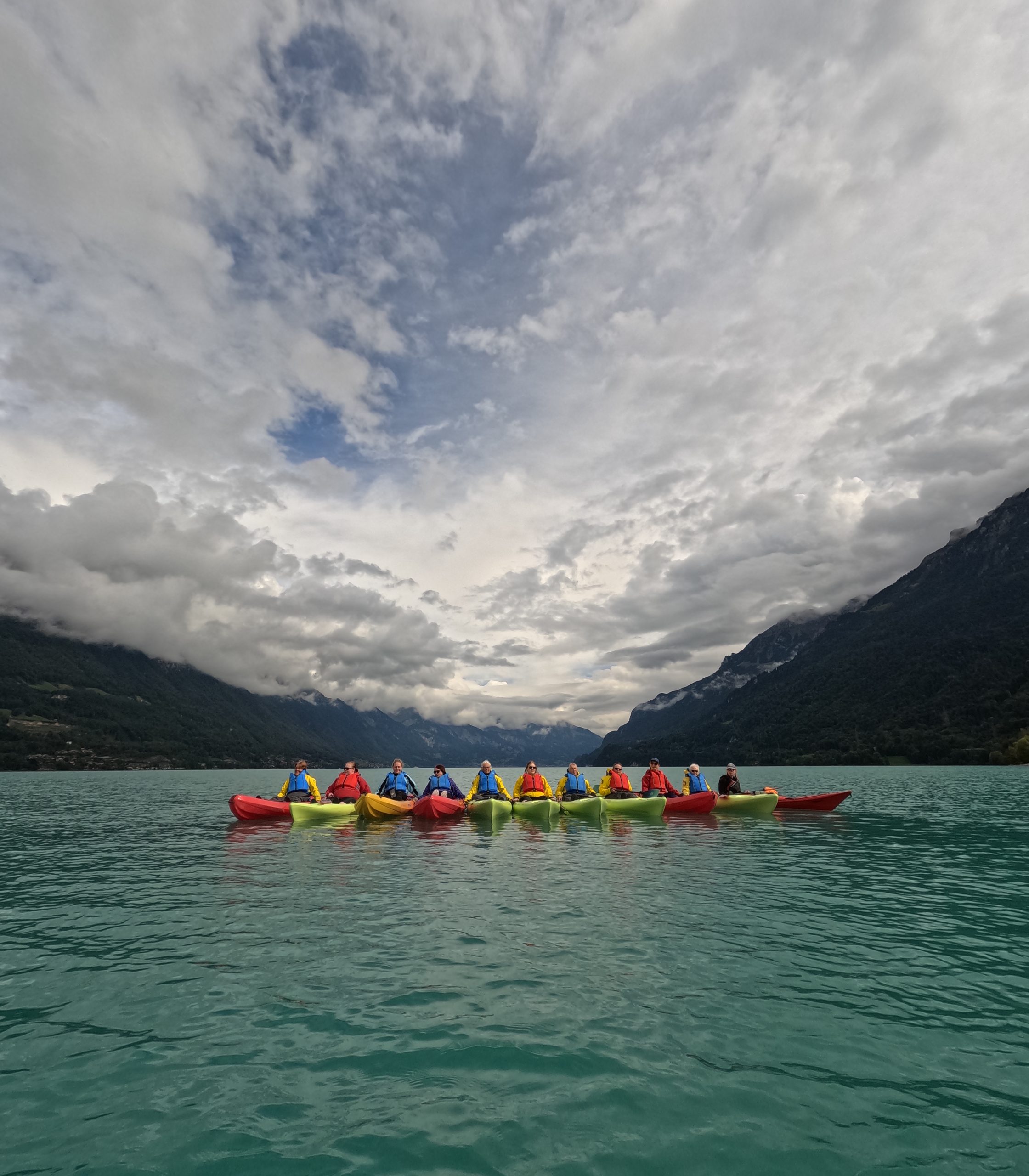 A group of women in colourful kayaks on a blue kale with mountains in the background